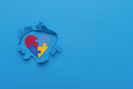 World Autism Awareness, concept with puzzle or jigsaw pattern on wooden heart in paper cut hole. Blue backgroundの写真素材