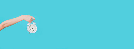 Kid holding alarm clock on blue background, closeup. Morning time. Time management, punctuality, awakening conceptの写真素材