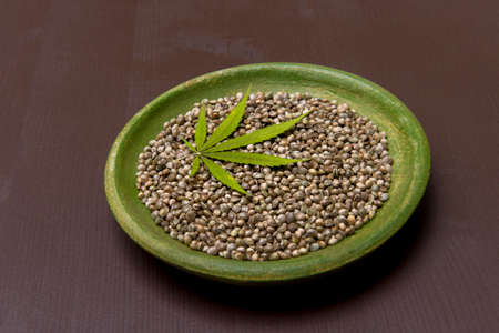 Green cannabis leaf and seeds on plate on wooden background. Vegetarian food conceptの写真素材