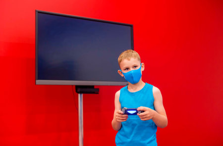 Little boy with mask playing video game in the red room. Television and video game addiction.