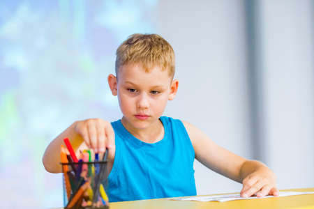Little boy sitting at desk and drawing with a color pen at  classroomの写真素材