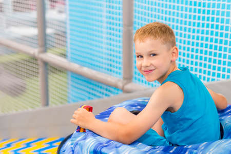Boy rolls on an inflatable ring on an artificial hill in trampoline club. Excited kid having fun at game centerの写真素材