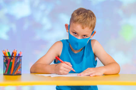 Little boy wear protective face mask sitting at desk and drawing with a color pen at  classroomの写真素材