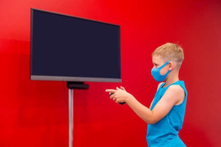 Little boy with mask playing video game in the red room. Television and video game addiction.の写真素材