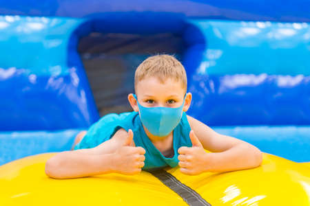 Child  with mask on colorful playground trampoline. Kids jump in inflatable bounce castle on kindergarten birthday party. Activity and play center for young child.の写真素材