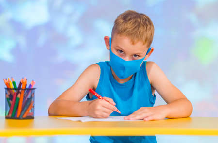 Little boy wear protective face mask sitting at desk and drawing with a color pen at  classroomの写真素材