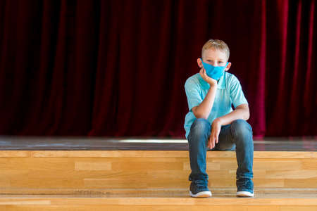 School kid with blue mask against virus and tablet at lesson. Safe back to school during pandemic concept. Social distancing to fight COVID-19の写真素材