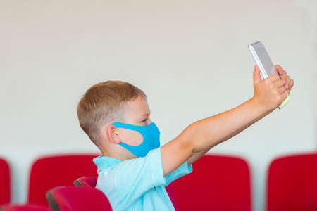 School kid with blue mask against virus and tablet at lesson. Safe back to school during pandemic concept. Social distancing to fight COVID-19の写真素材