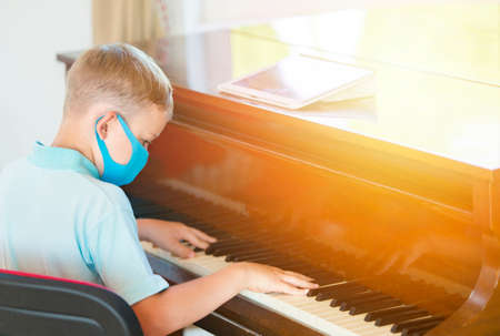 School kid with blue mask against virus and tablet at lesson. Safe back to school during pandemic concept. Social distancing to fight COVID-19の写真素材