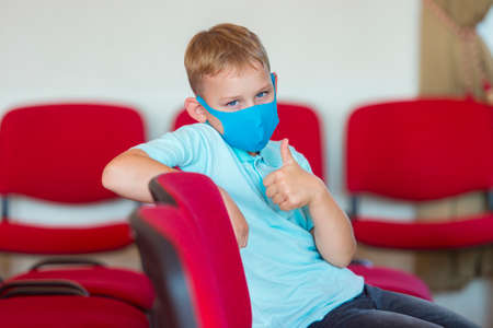 School kid with blue mask against virus and tablet at lesson. Safe back to school during pandemic concept. Social distancing to fight COVID-19の写真素材