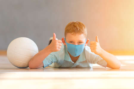 School kid with blue mask against virus and tablet at lesson. Safe back to school during pandemic concept. Social distancing to fight COVID-19の写真素材