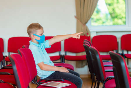 School kid with blue mask against virus and tablet at lesson. Safe back to school during pandemic concept. Social distancing to fight COVID-19の写真素材