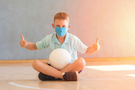School kid with blue mask against virus and tablet at lesson. Safe back to school during pandemic concept. Social distancing to fight COVID-19の写真素材