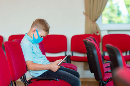 School kid with blue mask against virus and tablet at lesson. Safe back to school during pandemic concept. Social distancing to fight COVID-19の写真素材