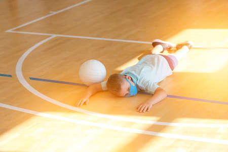 School kid with blue mask and  ball in a physical education lesson. Safe back to school during pandemic concept. Social distancing to fight COVID-19の写真素材