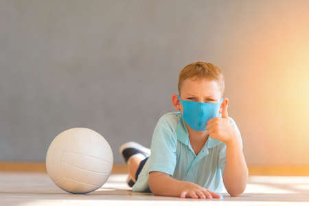 School kid with blue mask and  ball in a physical education lesson. Safe back to school during pandemic concept. Social distancing to fight COVID-19の写真素材