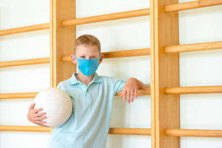 School kid with blue mask and  ball in a physical education lesson. Safe back to school during pandemic concept. Social distancing to fight COVID-19の写真素材