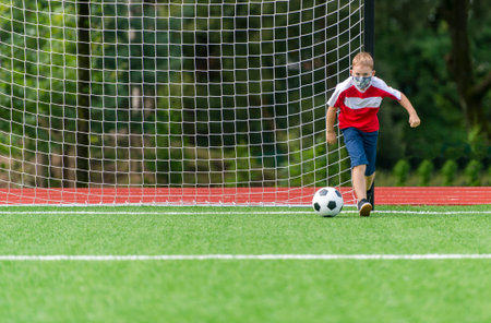 School kid with mask and soccer ball in a physical education lesson. Safe back to school during pandemic concept. Social distancing to fight COVID-19の写真素材