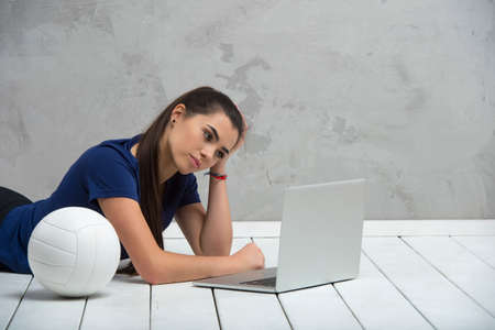 Young girl doing exercises with volleyball ball watching online tutorials on laptop. A sports coach leads an online lesson. Online workout concept.の写真素材