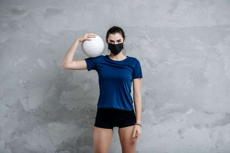 Young woman protective face mask with volleyball ball isolated on grey background. Protective masks against virus infection. Vintage color filterの写真素材