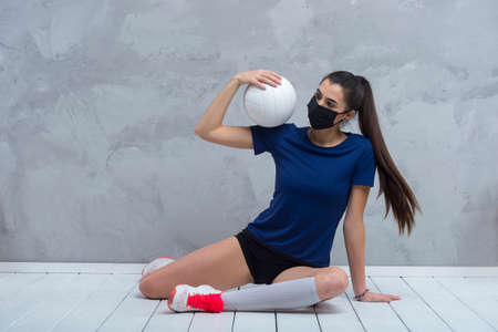 Young woman protective face mask with volleyball ball isolated on grey background. Protective masks against virus infection. Vintage color filterの写真素材