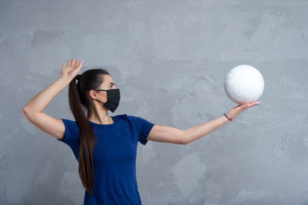 Young woman protective face mask with volleyball ball isolated on grey background. Protective masks against virus infection. Vintage color filterの写真素材
