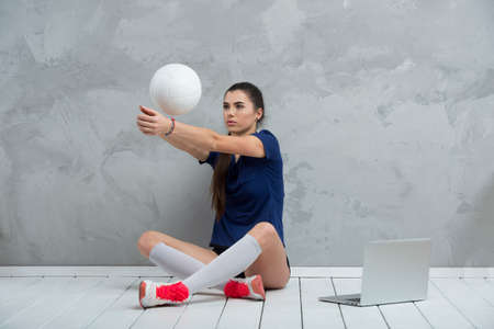 Young girl doing exercises with volleyball ball watching online tutorials on laptop. A sports coach leads an online lesson. Online workout concept.の写真素材