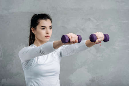 Young happy female doing fitness with dumbbels on grey background. Workout online concept. Vintage color filterの写真素材
