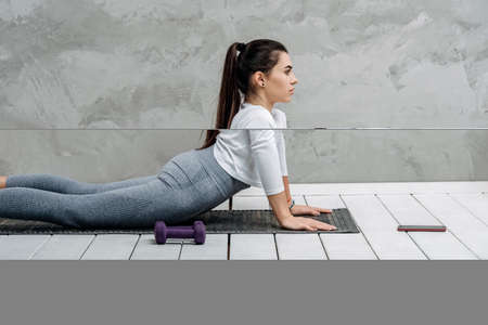 Young woman using smartphone during workout at home in the living room. Online personal trainer or on mobile phone. Workout online concept. Vintage color filterの写真素材