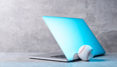 Baseball ball and grey laptop on grey background. Online workout concept
