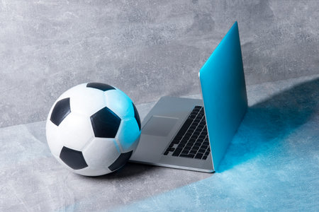 Soccer and football ball and grey laptop on grey background. Online workout concept