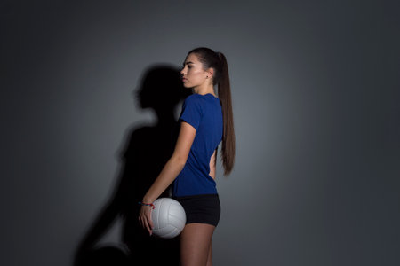 Volleyball girl hold and kick ball in blue costume on dark wall background. Player doing sport workout at home. Sport and recreation conceptの写真素材