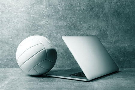 White Volleyball ball and grey laptop on grey background. Online workout concept. Green color filterの写真素材