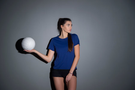 Volleyball girl hold and kick ball in blue costume on dark wall background. Player doing sport workout at home. Sport and recreation conceptの写真素材