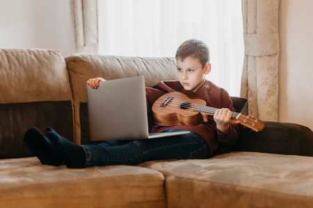 Boy playing ukulele and watching online course on laptop while practicing at home. Online training, online classes.Vintage color filterの写真素材
