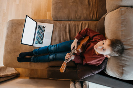 Boy playing ukulele and watching online course on laptop while practicing at home. Online training, online classes.Vintage color filterの写真素材