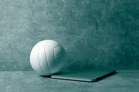 White Volleyball ball and grey laptop on grey background. Online workout concept. Green color filterの写真素材