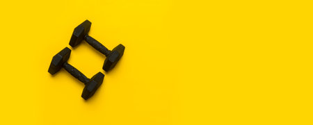 Black dumbbell on yellow background. Top view, space for your text.