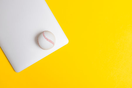 Baseball ball and grey laptop on yellow background. Online workout concept. Top view, space for your textの写真素材