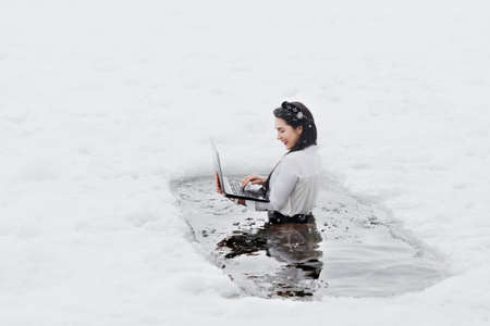 Girl with laptop in frozen lake ice hole. Woman hardening the body in cold water.の写真素材
