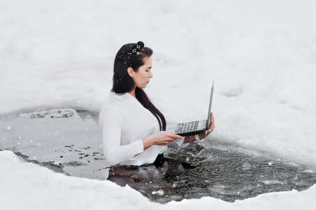 Girl with laptop in frozen lake ice hole. Woman hardening the body in cold water.の写真素材