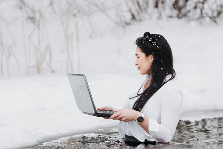 Girl with laptop in frozen lake ice hole. Woman hardening the body in cold water.の写真素材