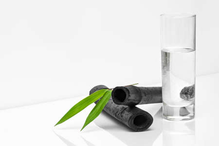 Bamboo charcoal water filter sticks, green leaf and glass of water. Natural bamboo charcoal is a powerful purifier which refreshes tap waterの写真素材