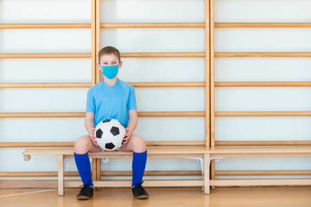 School kid with mask and soccer ball in a physical education lesson. Safe back to school during pandemic conceptの写真素材