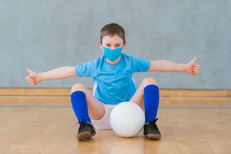 School kid with mask and volleyball ball in a physical education lesson. Safe back to school during pandemic conceptの写真素材