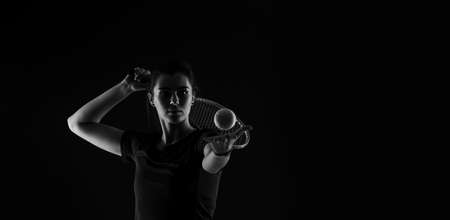 Tennis girl with racket serve ball on dark background. Player doing sport workout online. Sport and recreation concept. Black and white color filterの写真素材
