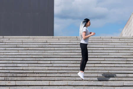 Fitness girl with african braids jumping on stairs during her morning workout. Urban sport conceptの写真素材