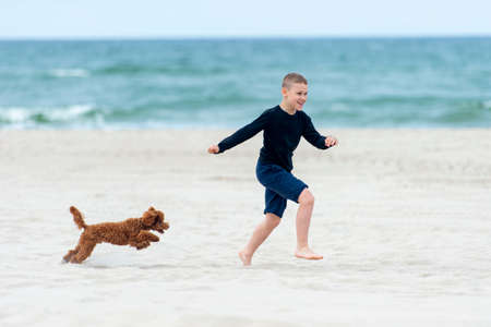 Happy boy running with her dog on the beach. Summer child's outdoor activitiesの写真素材