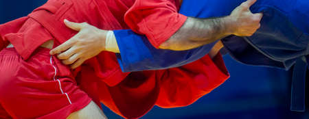 Two men in blue and red wrestling on a yellow wrestling carpet in the gym. Professional sport concept. Horizontal sport poster, greeting cards, headers, websiteの写真素材
