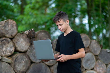 Boy with laptop in forest. Kid have online web lesson or class on computer at nature, green class. Back to school concept.の写真素材